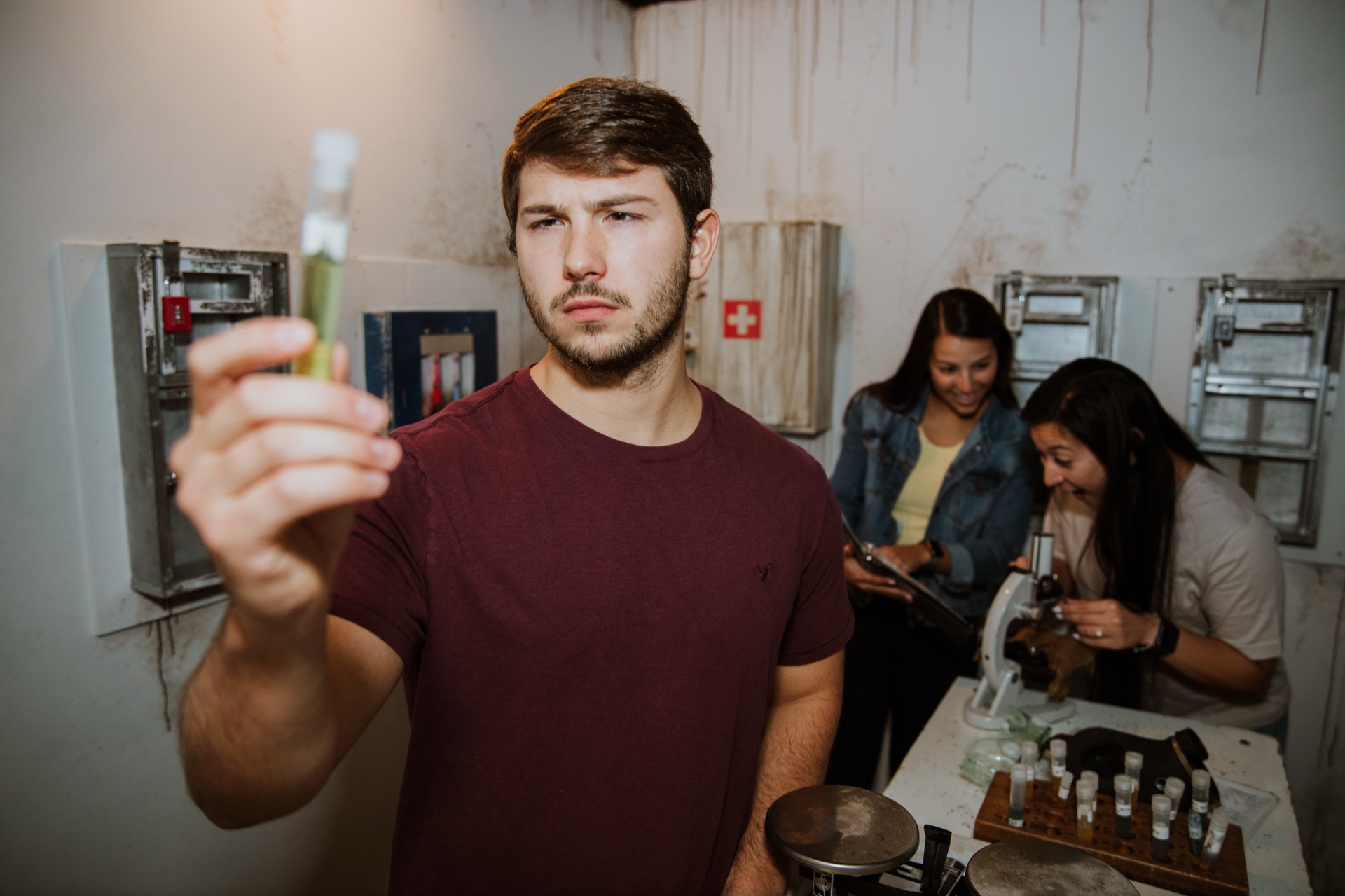 A player holds up a test tube while teammates work at a microscope inside the Vaccine: Search for the Cure lab